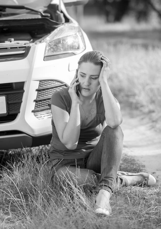 Black and white image of upset crying woman calling car service because of her broken automobile in field.