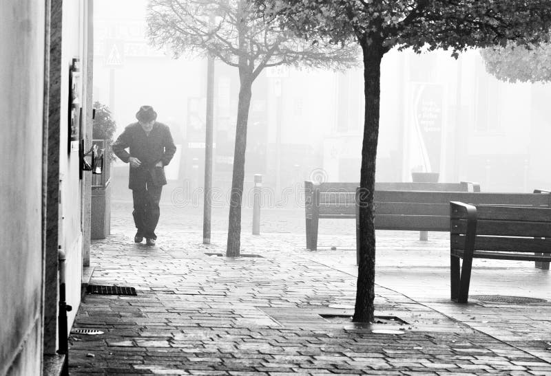 Black and white picture of a lonely old man walking alone in the park in the mist