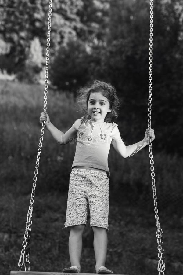 Black and white portrait of Cute little girl smiling on swing at summer day, Happy childhood concept stock image Black and white portrait of Cute little girl smiling on swing at summer day, Happy childhood concept stock image