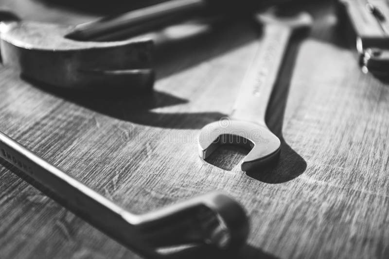 A black and white portrait of  a hammer, an open end and a box end wrench lying on a wooden table. The tools are being used to
