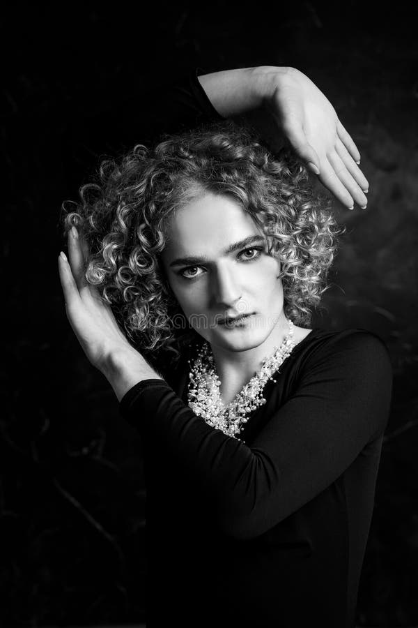 Black and white portrait of a sad androgyne guy model with blue eyes and blond hair in the image of a girl with beads around neck