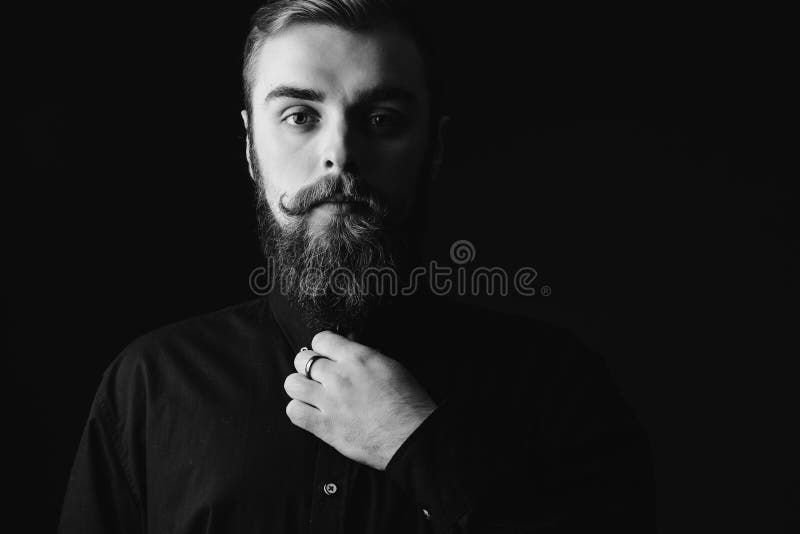 Black and white portrait of a stylish man with a beard and stylish hairdo dressed in the black shirt on the black royalty free stock photos Black and white portrait of a stylish man with a beard and stylish hairdo dressed in the black shirt on the black royalty free stock photos
