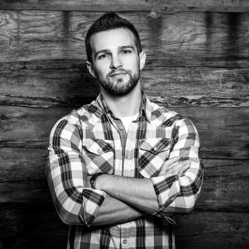 Black-white portrait of young handsome fashionable man against wooden wall