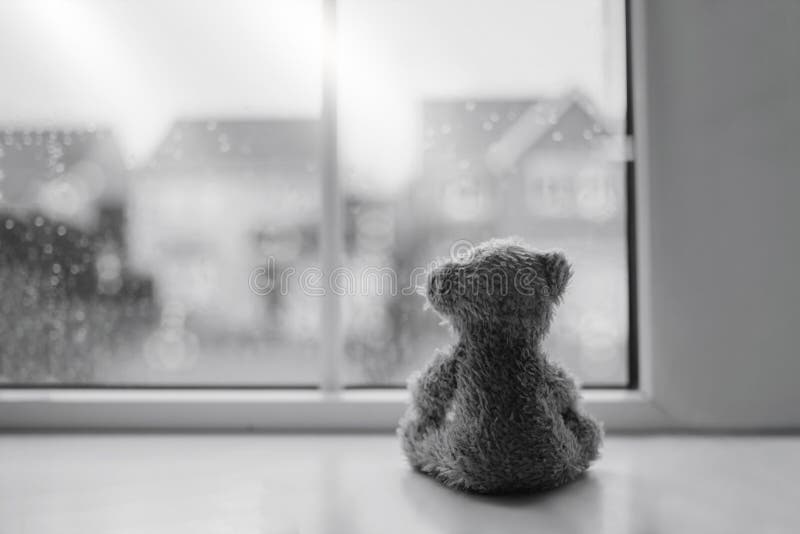 Black and white Rear view Lonely bear doll sitting alone looking out of window, Sad teddy bear sitting next to window in rainy day