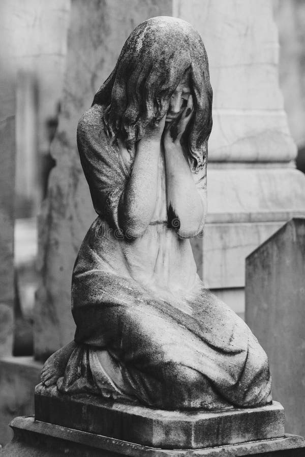 Black and white sculpture of a angel girl in an old cemetery. Closeup of stoned angel with closed eyes and cross monument at cemet