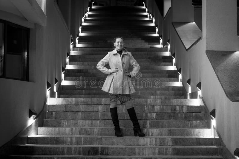 Black and white shot of elegant woman posing on stairs at night
