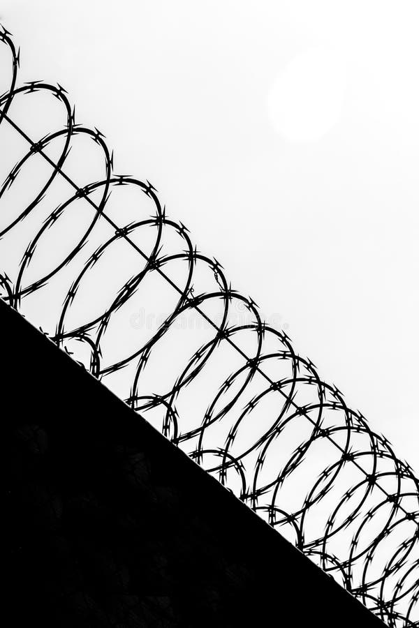 Black and white silhoutte of razor wire above solid wall low angle view looking up. Black and white silhoutte of razor wire above solid wall low angle view looking up