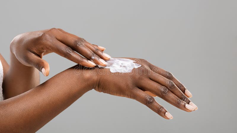 Skincare concept. Afro woman applying body lotion to her hands over gray studio background, panorama with free space. Skincare concept. Afro woman applying body lotion to her hands over gray studio background, panorama with free space