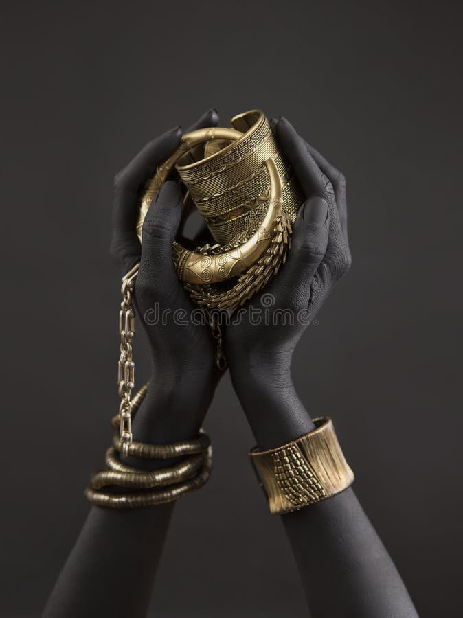 Black woman`s hands with gold jewelry. Oriental Bracelets on a black painted hand. Gold Jewelry and luxury accessories on black background closeup. High Fashion art concept