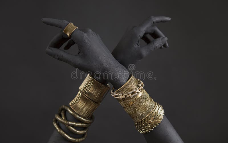 Black woman`s hands with gold jewelry. Oriental Bracelets on a black painted hand. Gold Jewelry and luxury accessories on black background closeup. High Fashion art concept