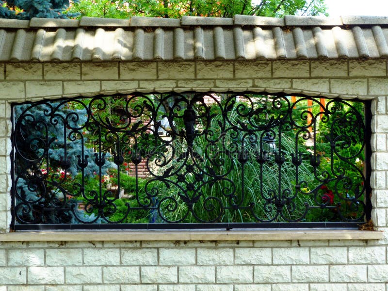 Black wrought iron fence in white concrete wall and lush green garden royalty free stock images Black wrought iron fence in white concrete wall and lush green garden royalty free stock images