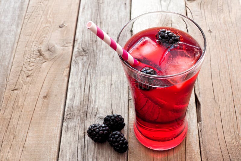 Blackberry fruit drink in a glass with straw over a rustic wooden background. Blackberry fruit drink in a glass with straw over a rustic wooden background