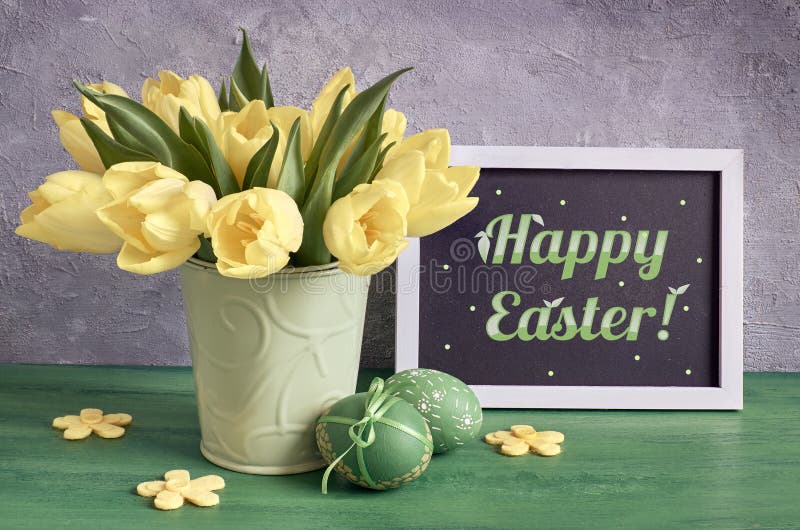 Blackboard with caption \'Happy Easter\' with yellow tulips and green Easter eggs royalty free stock images