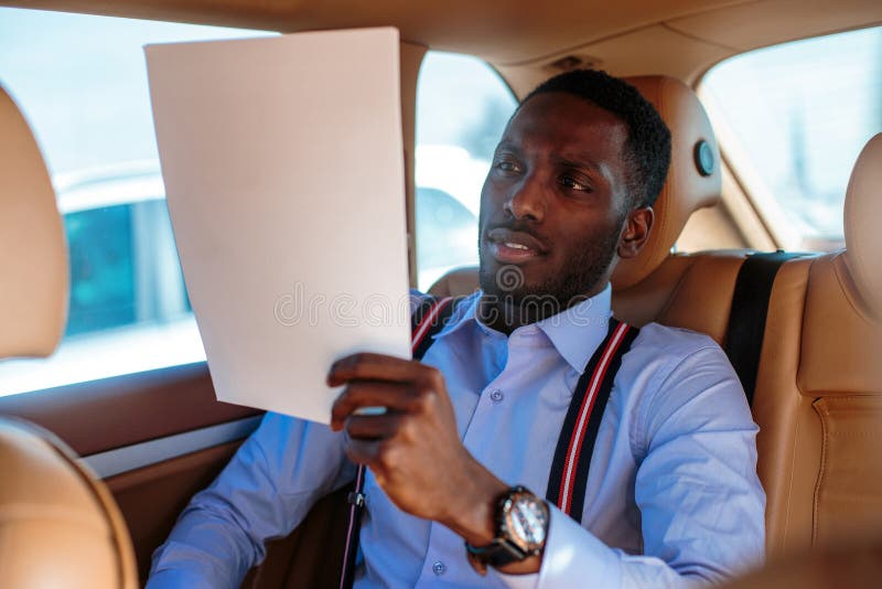 Blackman in una camicia blu si siede sul sedile posteriore del ` s dell'automobile immagini stock libere da diritti Blackman in una camicia blu si siede sul sedile posteriore del ` s dell'automobile immagini stock libere da diritti