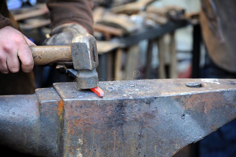 Blacksmith working metal with hammer on the anvil