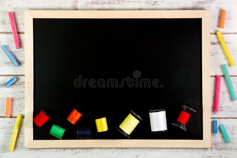 Blank blackboard and sewing threads on wooden table. Template mock up for adding your design and leave space beside frame for royalty free stock image