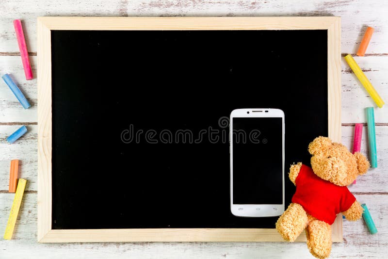 Blank blackboard, Teddy Bear and smart phone on wooden table. Template mock up for adding your design and leave space beside frame stock images