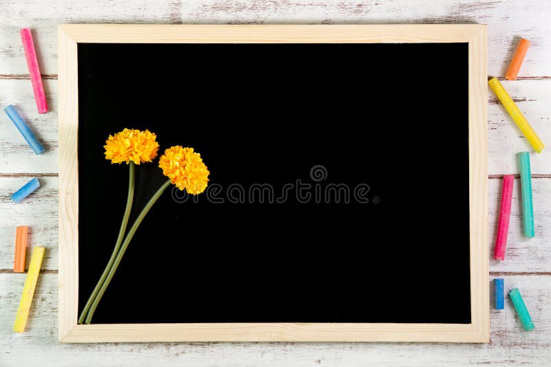 Blank blackboard and Yellow plastic flowers on wooden table. Template mock up for adding your design and leave space beside frame royalty free stock photos