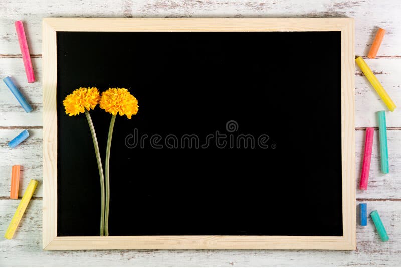 Blank blackboard and Yellow plastic flowers on wooden table. Template mock up for adding your design and leave space beside frame royalty free stock image