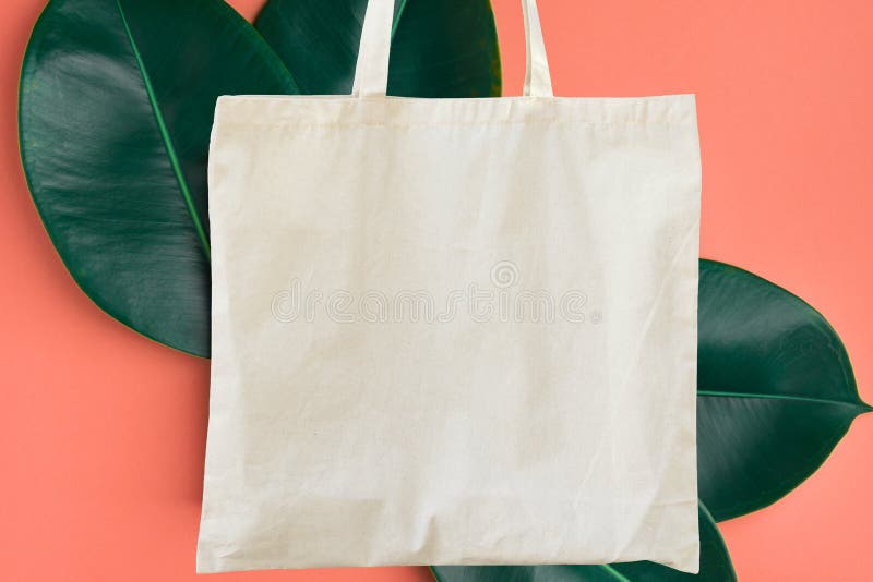 Blank cotton shite shopper tote bag on pink background with green leaves. Mock up template for product branding plastic free