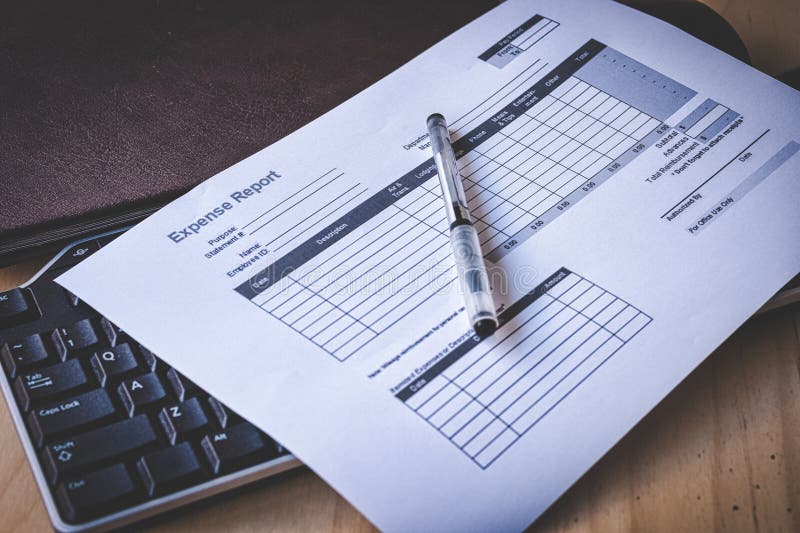 Blank Expense Report on Black Keyboard and Brown Leather Notebook on Pine Desk royalty free stock photo