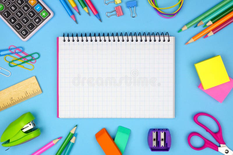 Blank graphing paper notebook with school supplies frame against blue. Back to school. Copy space.