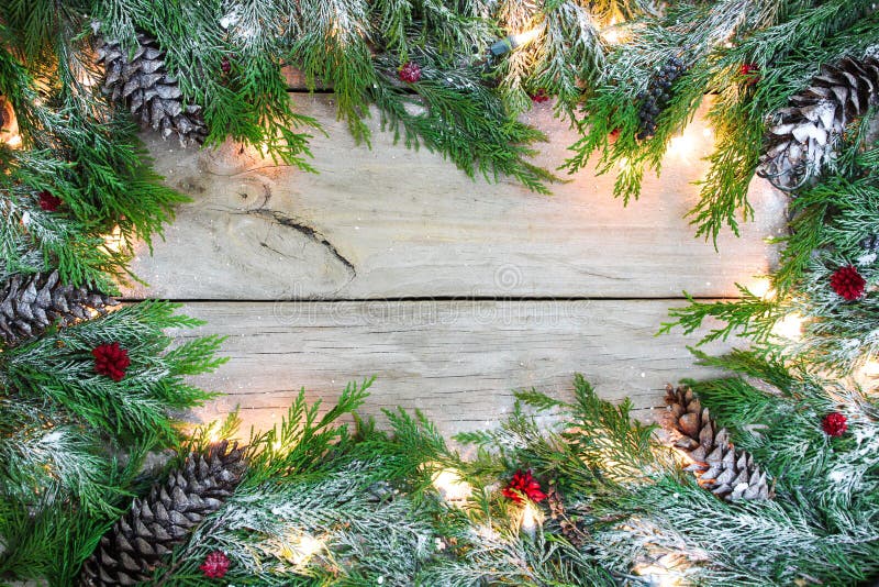 Christmas tree garland border with snow, lights, pine cones and berries on antique rustic wooden background. Christmas tree garland border with snow, lights, pine cones and berries on antique rustic wooden background