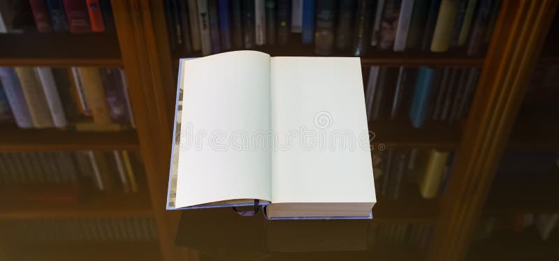Blank open book to write your text, on a glass table with a reflection of the bookcase on the back. Copy space stock image