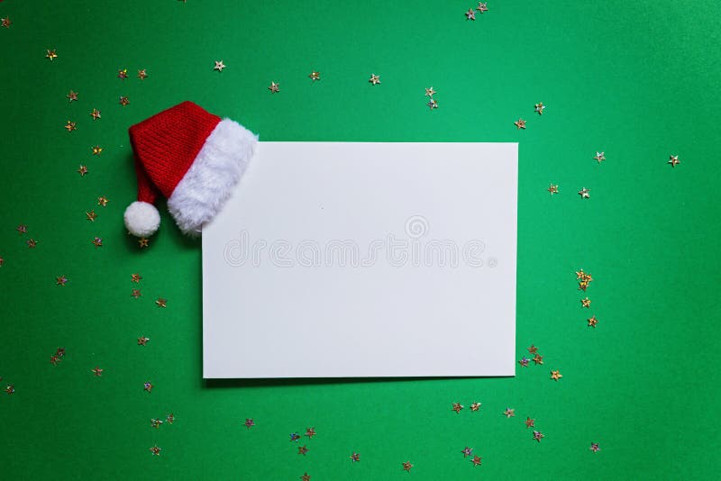 Blank of paper with red Santa hat on green background with confetti. new year concept. Greeting card, xmas celebration 2020. Flat. Paper blank with Santa hat on royalty free stock photo Blank of paper with red Santa hat on green background with confetti. new year concept. Greeting card, xmas celebration 2020. Flat. Paper blank with Santa hat on royalty free stock photo