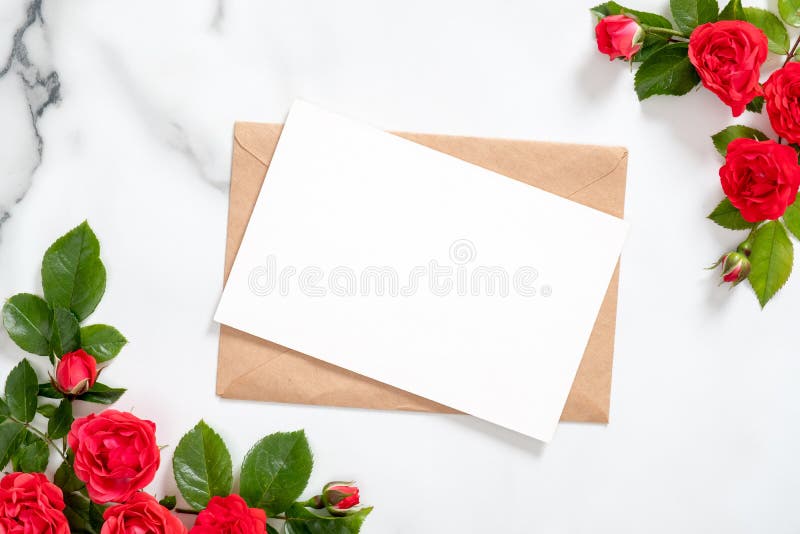 Blank postcard with rose flowers frame and craft paper envelope on marble background. Greeting card mockup for Valentine`s Day