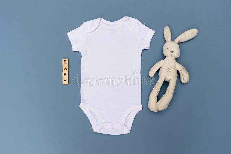 Blank white baby bodysuit grow mockup with cream rabbit soft toy and `baby` written in wooden tiles on a light blue background. Newborn clothes digital mock