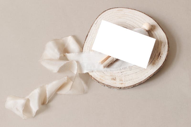 Blank white business card mockup on wooden plate with spool and silk ribbon. Beige table backgound. Branding identity.