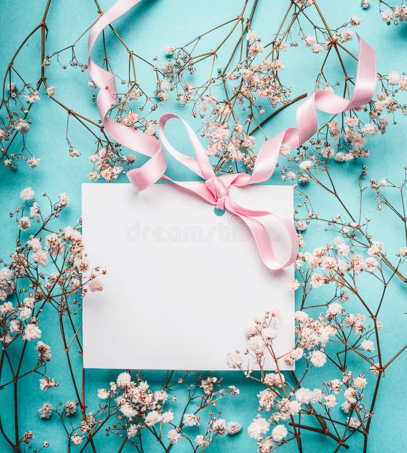 Blank white greeting card with pink ribbon on little white flowers at turquoise blue background