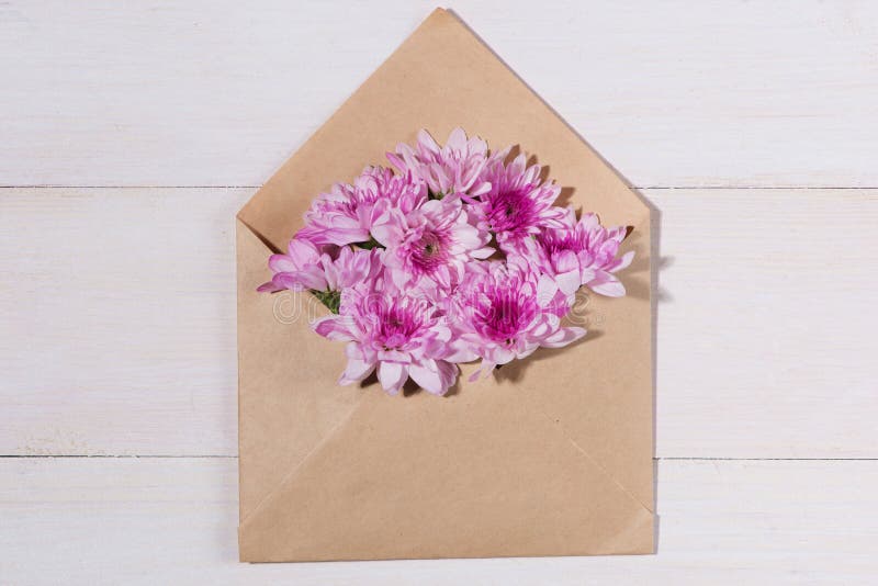 Blank white paper tag with brown envelope and pink flowers on wooden table.