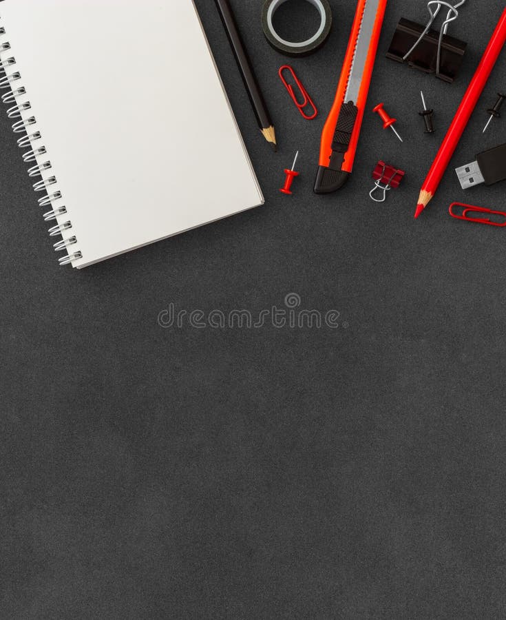 White spiral paper notebook with cutter knife, paper clumps, paper clips, push pins, colored pencils on dark background royalty free stock image