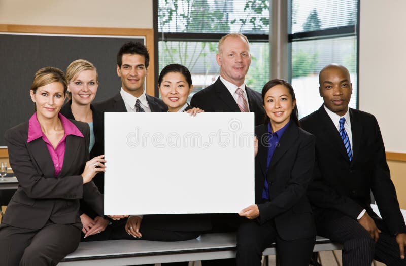 Multi-ethnic co-workers posing with blank sign in conference room. Multi-ethnic co-workers posing with blank sign in conference room