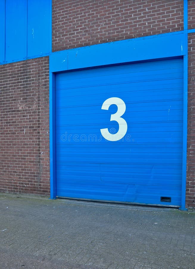 Blue colored sectional door in an old building with a brick facade. On the door is a white digit 3 (three). Blue colored sectional door in an old building with a brick facade. On the door is a white digit 3 (three).