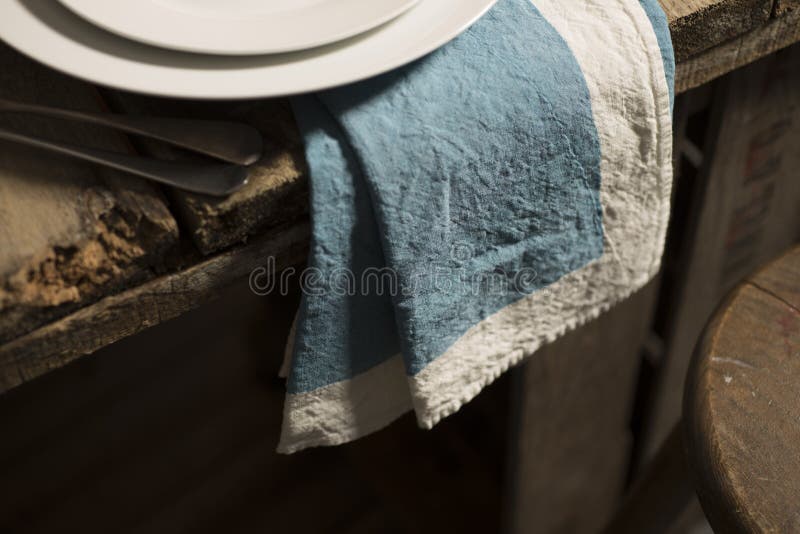 Blaue Tafelserviette, die vom Rand des Holztischs baumelt lizenzfreie stockfotos Blaue Tafelserviette, die vom Rand des Holztischs baumelt lizenzfreie stockfotos