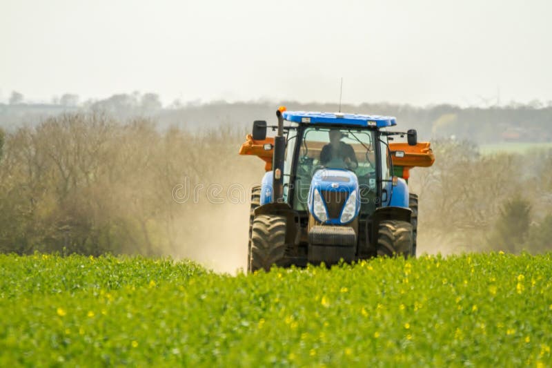 A modern new holland tractor spreading fertilizer in english crop field with dust trail. A modern new holland tractor spreading fertilizer in english crop field with dust trail