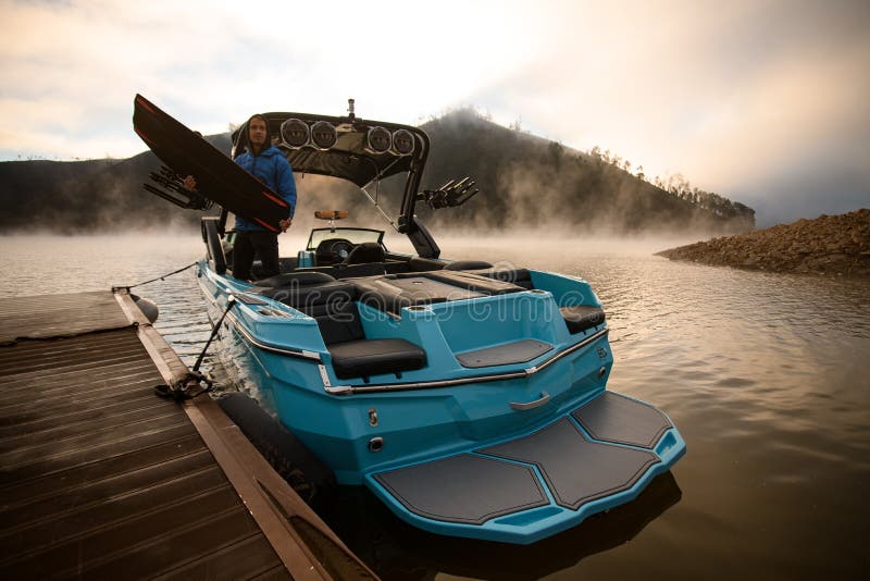 Blaues Boot, das am Steg festgemacht wurde, und ein Mann mit einem Wakeboard in den Händen lizenzfreie stockfotos