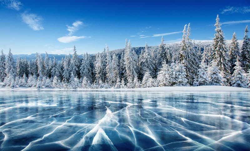 Blauwe ijs en barsten op de oppervlakte van het ijs Bevroren meer onder een blauwe hemel in de winter De heuvels van pijnbomen De