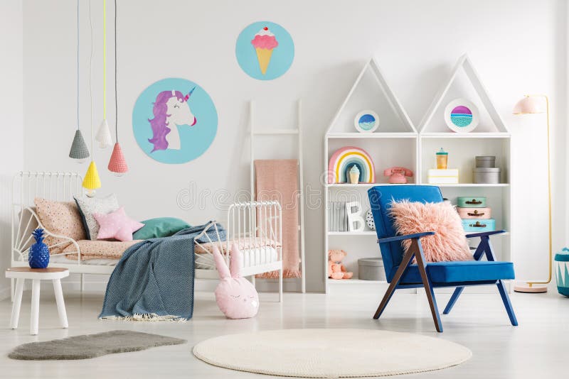 Blauwe leunstoel naast bed met deken in kleurrijke kind` s bedro stock foto Blauwe leunstoel naast bed met deken in kleurrijke kind` s bedro stock foto