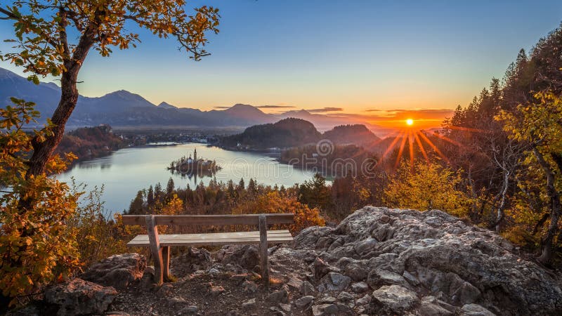 Bled, Slovenia - Beautiful panormaic skyline autumn view with hilltop bench and tree and colorful sunrise of Lake Bled