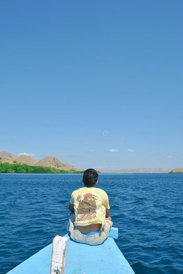 Blicke hinter einem jungen Mann, der auf einem Schiff im Meer um die Komodo-Insel sitzt lizenzfreie stockbilder Blicke hinter einem jungen Mann, der auf einem Schiff im Meer um die Komodo-Insel sitzt lizenzfreie stockbilder
