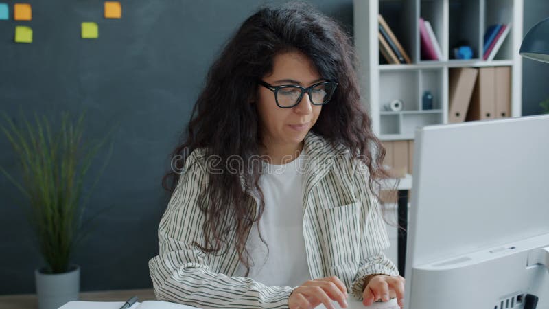 Blije jonge vrouw die van de werkresultaten geniet die het computerscherm bekijkt dat handen klapt die glimlachen op kantoor