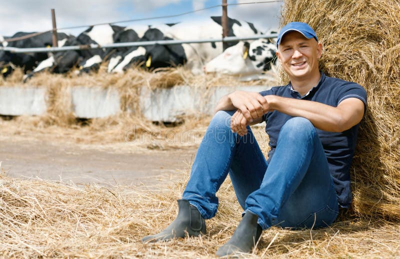 Blije landbouwer op een landbouwbedrijf onder koeien die op grond zitten royalty-vrije stock afbeelding Blije landbouwer op een landbouwbedrijf onder koeien die op grond zitten royalty-vrije stock afbeelding