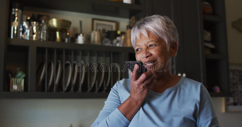 Blije vrouw met gemengde wedloop die over smartphone in de keuken spreekt