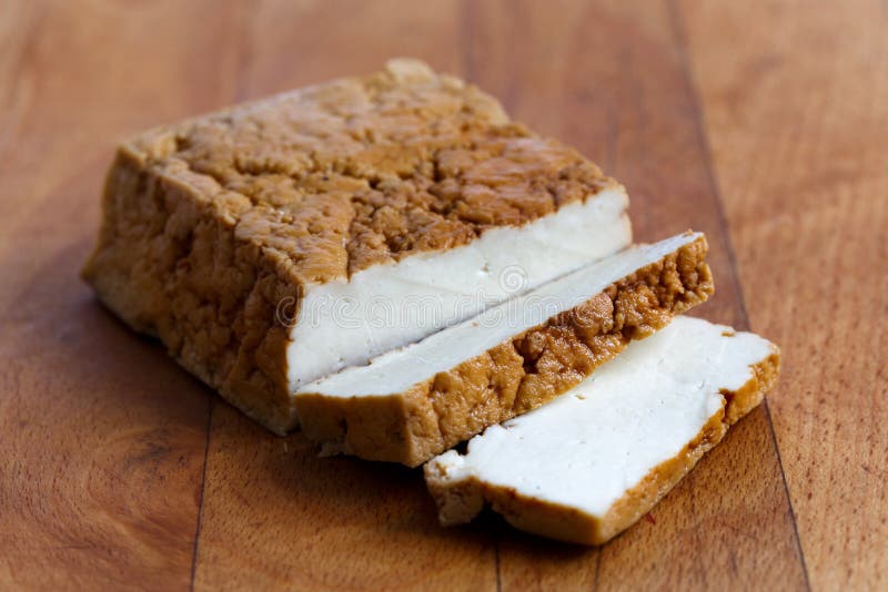 Bloc de tofu fumé et de deux tranches de tofu sur le verrat de hachage en bois photographie stock libre de droits Bloc de tofu fumé et de deux tranches de tofu sur le verrat de hachage en bois photographie stock libre de droits