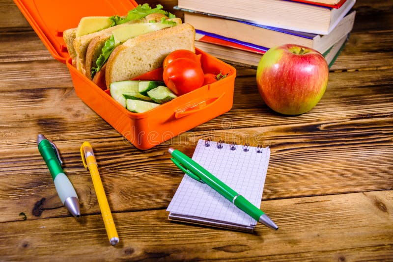 Bloc-notes, stylos, pomme mûre, pile de livres et gamelle avec des sandwichs, des concombres et des tomates sur la table en bois photos stock Bloc-notes, stylos, pomme mûre, pile de livres et gamelle avec des sandwichs, des concombres et des tomates sur la table en bois photos stock