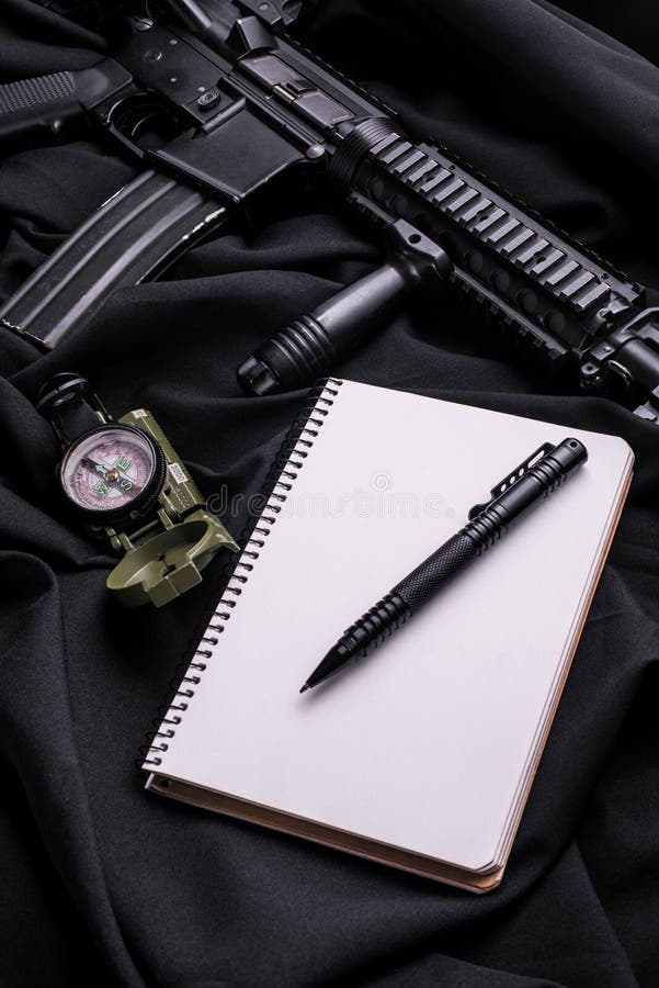 Bloco de notas com a pena no pano preto com rifle e compasso foto de stock